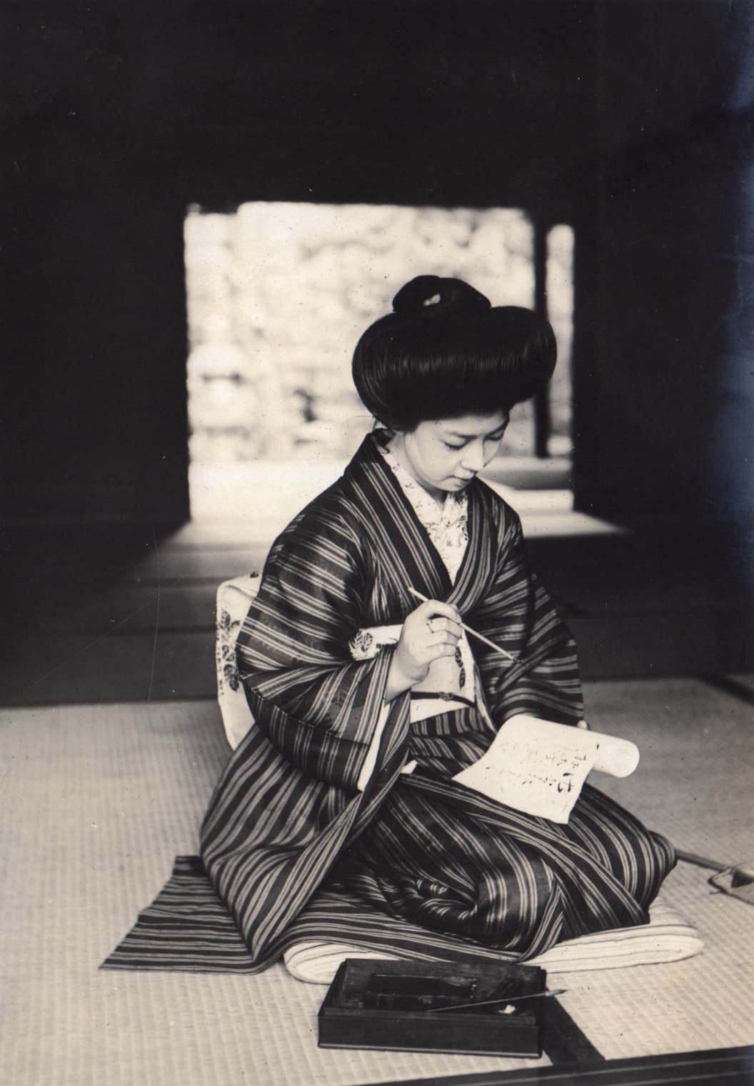 A 1911 photograph of a woman writing with a brush on a paper roll